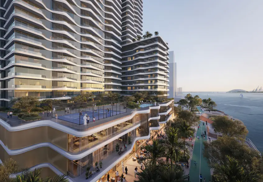 Modern high-rise waterfront building with wavy balconies, a rooftop sports court, and a palm-lined pedestrian promenade along the sea.